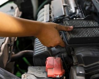 An auto mechanic wearing protective work gloves holds a dirty, clogged air filter