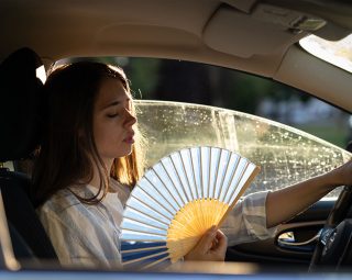 Exhausted young woman driver with hand fan suffering from heat in car