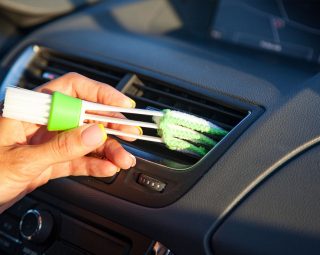 Female hand with a brush for wiping dust on the dashboard of the car