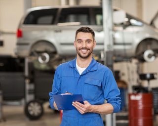 Happy mechanic man with clipboard at car workshop