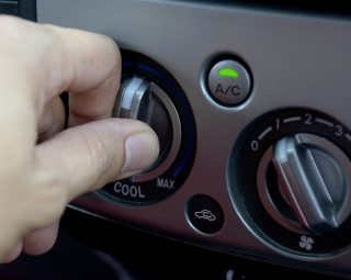 Left hand adjusting a temperature control knob of the car's air conditioning system