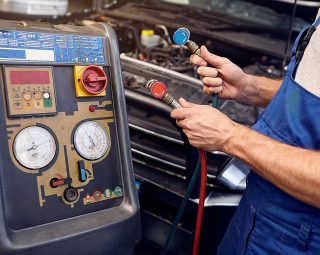 Mechanic holds a set of high-pressure pipes for filling the car's air conditioning system.