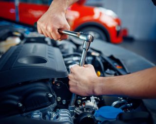 Worker in uniform disassembles vehicle engine, car service station. Automobile checking and inspection, professional diagnostics and repair