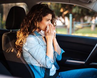 Young woman driving car with protective mask on her face