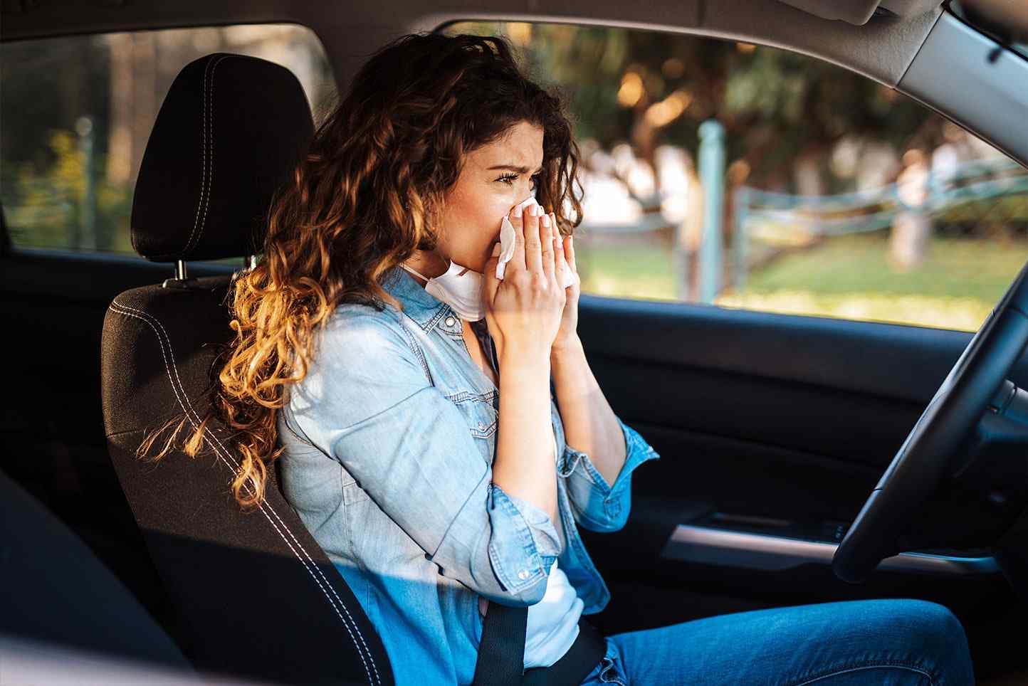 Young woman driving car with protective mask on her face