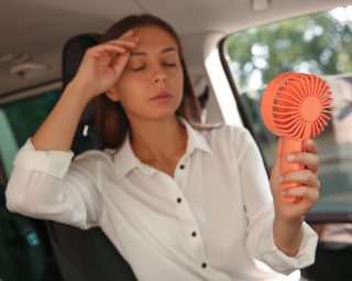 Young woman with portable fan suffering from heat in car